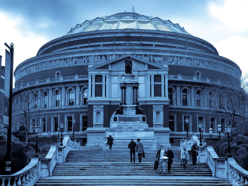A grand domed red brick concert hall lit up on a summer evening