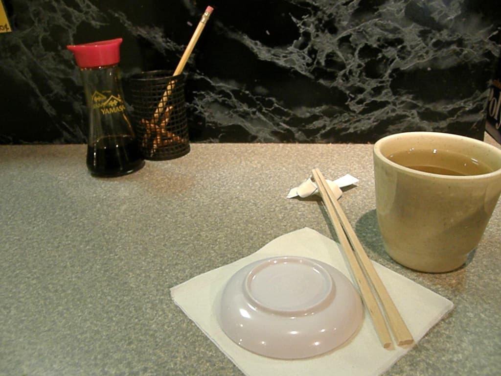 A sushi chef preparing nigiri at a pale wooden omakase counter